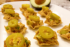 mini chicken taco bites on a plate served with avocado and topped with sliced jalapeno peppers