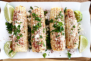 Mexican street corn on a plate with sliced limes on the side