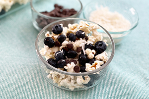 a bowl of popcorn with blueberries, toasted coconut and chocolate chips